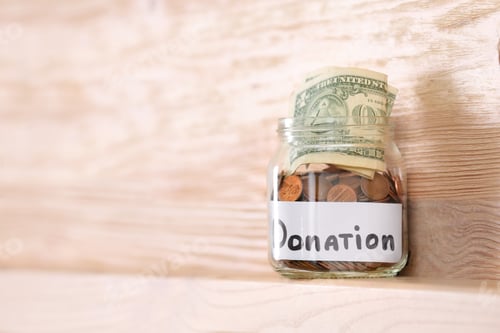 Preview: Glass jar with money and label DONATION on shelf against wooden background. Space for text