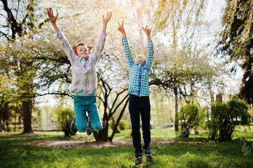 Preview: Two brother boy with headphones having fun and jump in air on park. Brother love.