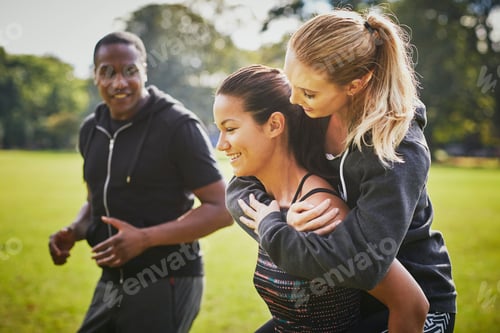 Preview: Personal trainer encouraging two women piggy backing in park