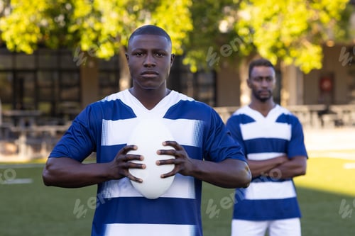Preview: Two African American young male athletes are holding a rugby ball on a field outdoors
