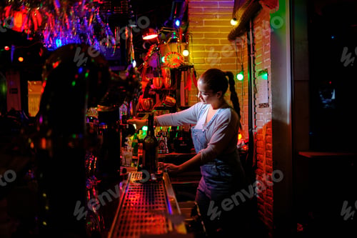 Preview: Female bartender prepares a cocktail while working behind the counter of a bar.