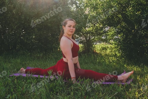Preview: young beautiful woman in red leggings and a top practicing yoga in a city park