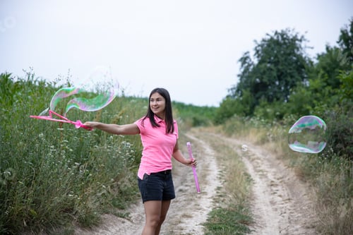 Preview: Young woman plays with big soap bubbles in a field among the grass.