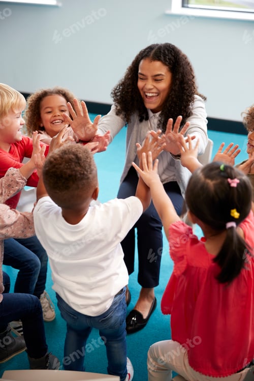 Preview: Infant school children in a circle in the classroom giving high fives to their teacher