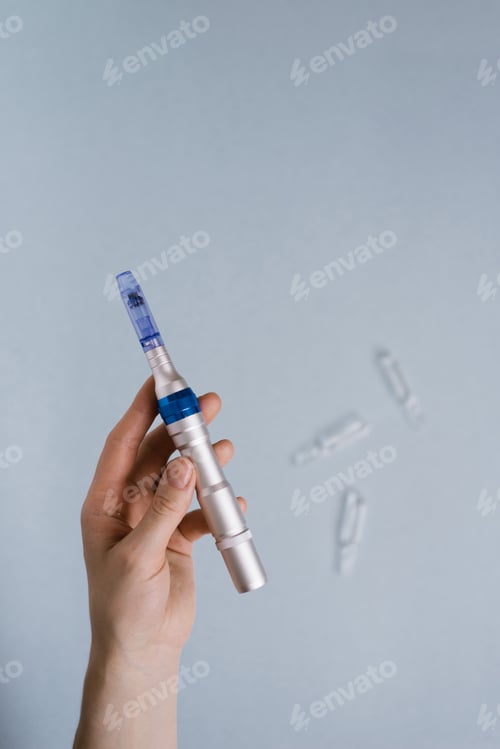 Preview: Fractional Mesotherapy Device in the Cosmetologist's Hand and Ampoules of Serum for the Skin