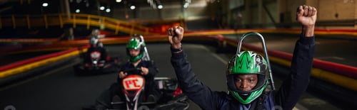 Preview: excited african american go cart driver in helmet raising hands and winning race, go-kart banner