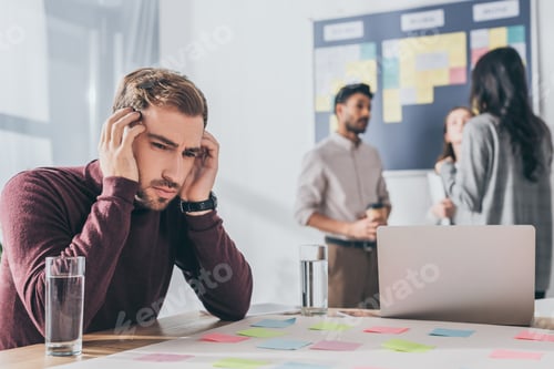 Preview: selective focus of tired businessman with headache near coworkers