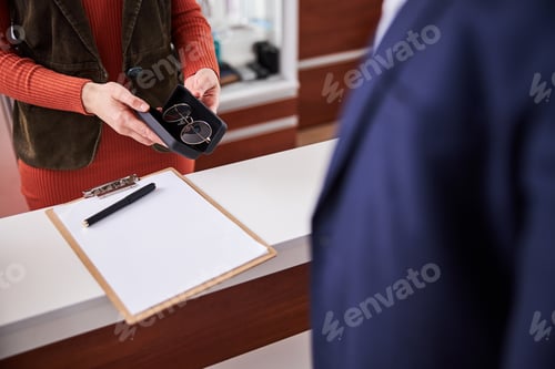 Preview: Caucasian eyewear consultant giving prescription glasses to a buyer