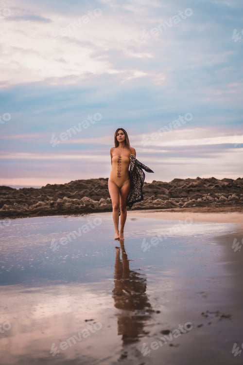 Preview: A brunette woman with a swimsuit and a pareo walking along the beach in summer in the cloudy sunset