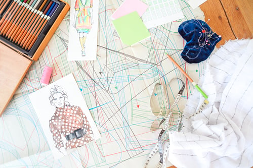 Preview: Table of the tailor with fabric, sketches and sewing equipment