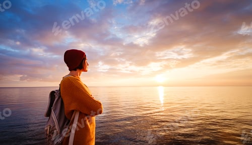 Preview: A charming calm young woman stands by the sea expressing delight. banner