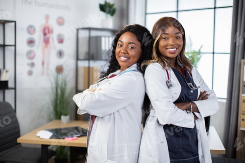 Preview: Two beautiful young female black skinned african doctors, standing back to back with arms crossed