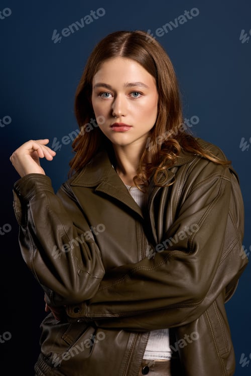 Preview: Young woman poses in autumn fashion with brown leather against a blue backdrop