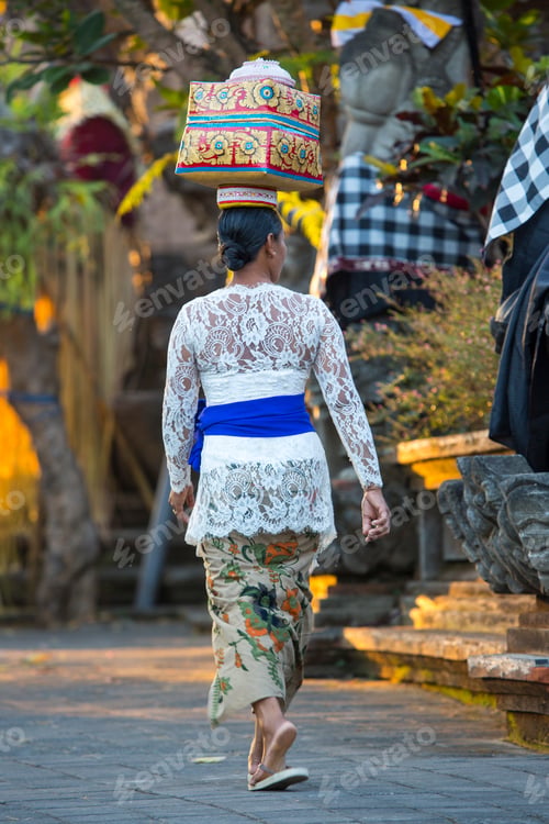 Preview: A woman in traditional Balinese attire walking gracefully through a temple courtyard.