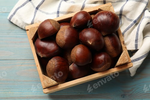 Preview: Roasted edible sweet chestnuts in crate on light blue wooden table, top view