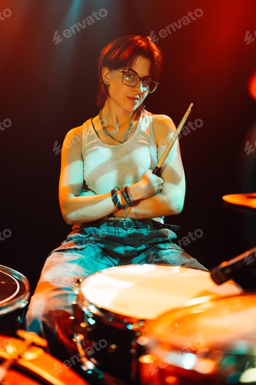 Preview: Young drummer posing with drumsticks on stage under colorful lights