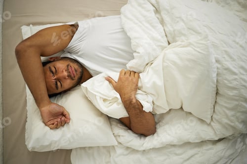 Preview: Im struggling to fall asleep. Shot of a young man frowning while lying in his bed.