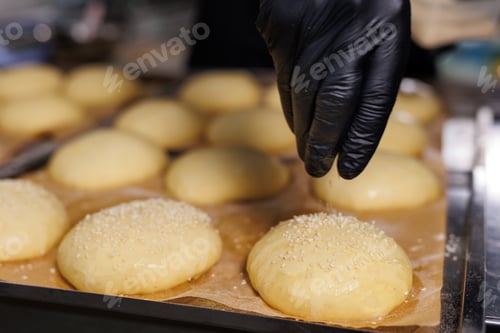 Preview: Close-up of the chef's gloved hands, who sprinkles sesame seeds on burger buns before baking.