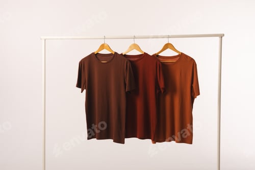 Preview: Three brown t shirts on hangers hanging from clothes rail and copy space on white background