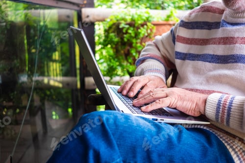 Preview: Senior man sitting outdoor in wooden balcony while using laptop computer.