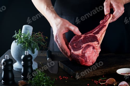 Preview: Chef cutting steak beef. Mans hands hold raw steak Tomahawk on rustic wooden cutting board on black