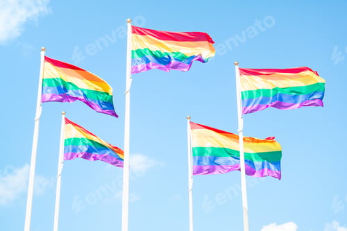 Preview: Rainbow LGBT flags waving on sky background with clouds, horizontal closeup