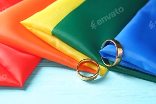 Preview: Wedding rings and rainbow flag on wooden table. Gay marriage