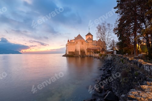 Preview: Stunning castle on an elevated hill overlooking a tranquil lake during a sunset in Lake Tir, Austria