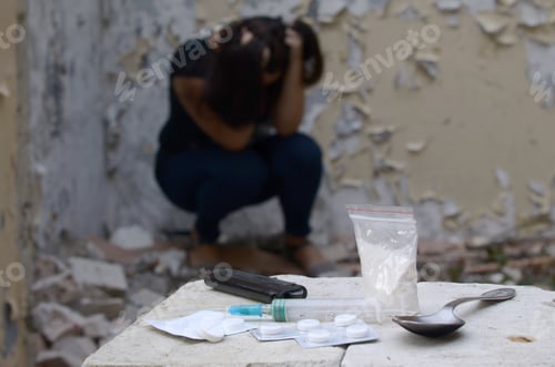 Preview: Young woman in despair suffers from narcotic effects next to packs of heroin and many drug tablets