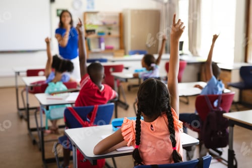 Preview: Rear view of students raising their hands while sitting on their desk in the class at school