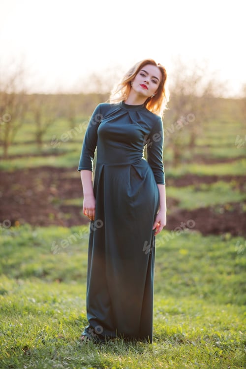 Preview: Yong elegance blonde girl at green dress on the garden in spring on sunset.