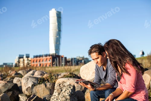 Preview: Young couple using digital tablet on rocks with Turning Torso skyscraper in background