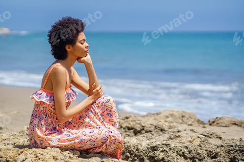 Preview: Young black woman sitting on rocks on the beach, eyes closed, relaxing with mindfulness techniques.