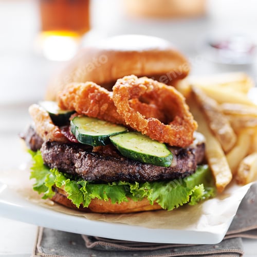 Preview: bacon barbecue burger topped with onion rings on white table served with fries