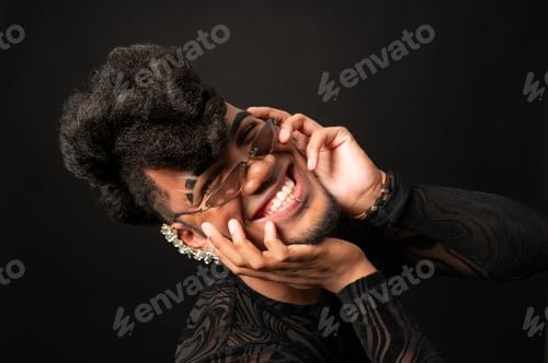 Preview: Young model smiling and touching sunglasses while posing in studio with black background
