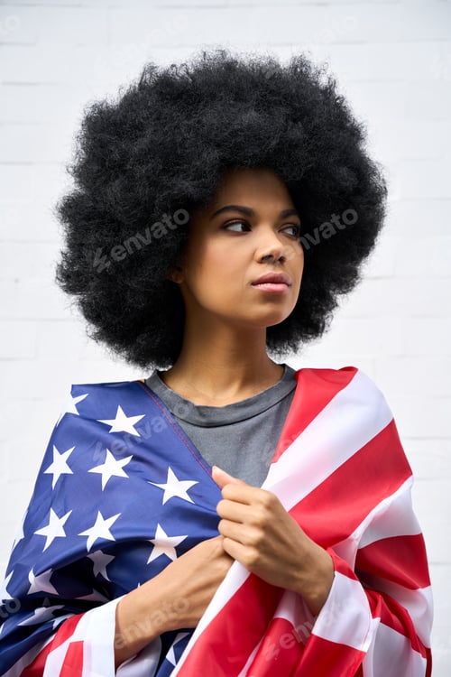 Preview: Thoughtful Afro American girl wrapped in usa flag standing on white background.