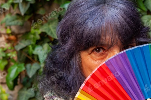 Preview: Hispanic senior female posing with a hand fan with the LGBT flag colors