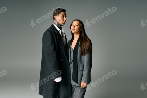 Preview: Young couple in stylish gray outfits standing close together in a modern studio setting