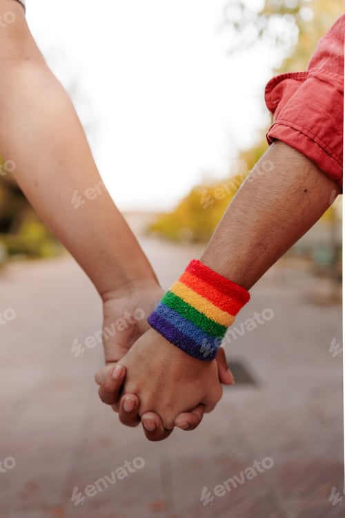 Preview: Latin trans woman and partner holding hands showing rainbow wristband