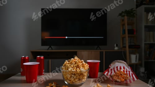 Preview: Glass bowl of popcorn and plastic cups on wooden table with television.