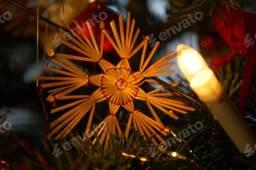 Preview: Light bulb on the Christmas tree illuminating a rustic straw toy in the shape of a snowflake