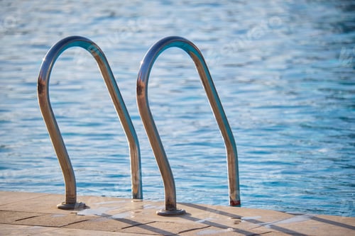 Preview: Close up of swimming pool stainless steel handrail descending into tortoise clear pool