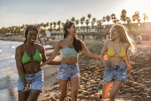 Preview: Three multiracial friends running and laughing in the beach in a summer day