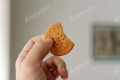 Preview: Selective focus of a person holding a bitten cookie under the lights with a blurry background