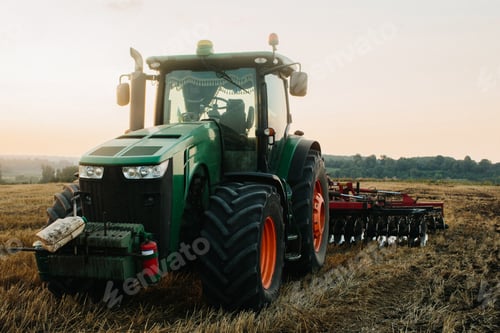 Preview: Close up photo of a modern green tractor with red disc plow working with GPS for precision farming.
