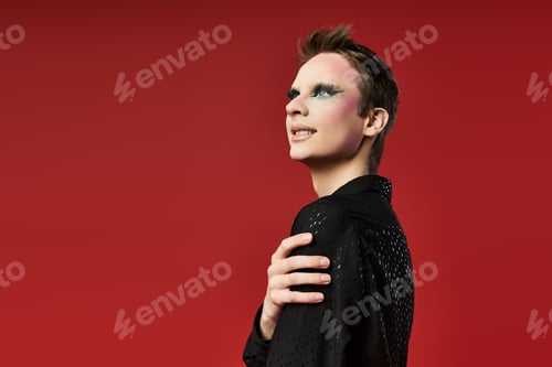 Preview: Young Drag Artist Poses Confidently Against Bold Red Background in Stylish Attire