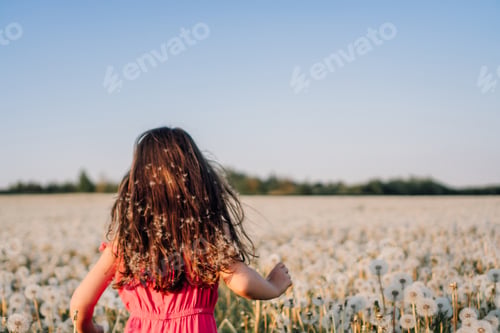 Preview: Happy little girl with brown hair running in meadow full of white, fluffy dandelions