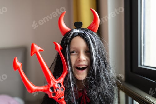 Preview: Little Girl in costume of devil with red horns at home. Happy Halloween concept