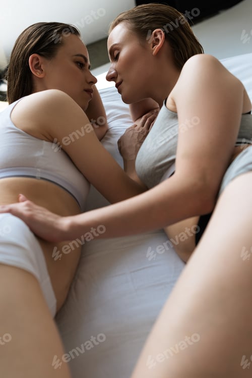 Preview: young woman touching sexy lesbian girlfriend while lying on white bedding