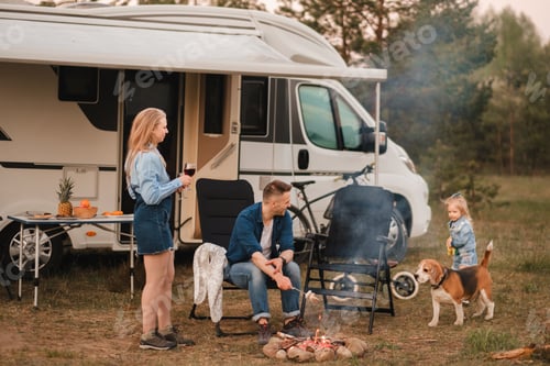 Preview: A family cooks sausages on a bonfire near their motorhome in the woods
